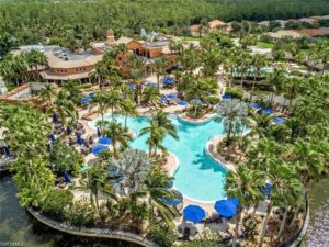 A resort pool with palm trees and blue umbrellas.