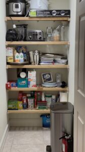 A shelf with many items on it and a trash can